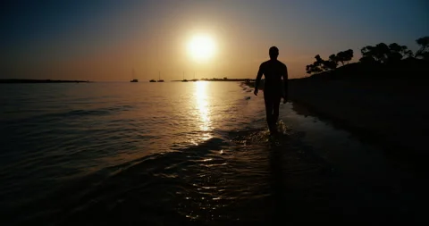 Silhouette of Man Walking Away Along Beach at Sunset Stock Footage 343596108