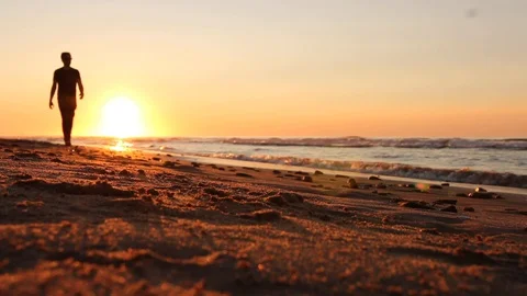 Silhouette of a man walking on a beach at sunset Stock Footage 129713604