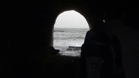 Silhouette of a man walking with a dog to the exit of a cave into the sea. Stock Footage 89689927