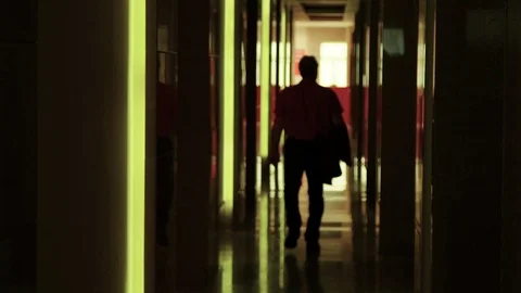 Silhouette man walking down lit up yellow hallway  Stock Footage 108064466