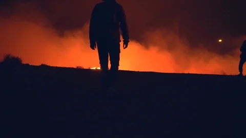 Silhouette of a man walking to the edge of a cliff, revealing burning Stock Footage