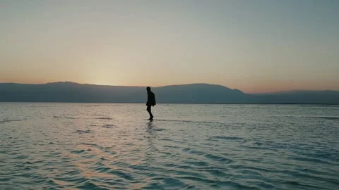 Silhouette of man walking in shallows of Dead Sea in Israel at sunset. Stock Footage 257865514
