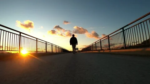 Silhouette of man walking through a bridge at sunset in rear view Stock-Footage 148502401
