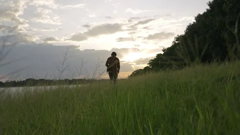Silhouette of Man Walking Through Grass at Lakeside Sunset 스톡 동영상 314707063