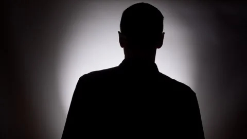 A silhouette of a man walking toward a light in a dark room.  Stock Footage 325593891