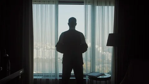 The silhouette of a man wearing a jacket in front of a window Stock Footage 124114376