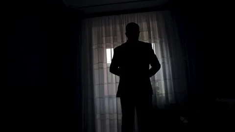 Silhouette of a man wears a jacket standing in front of the window of the hotel Stock Footage 213596792