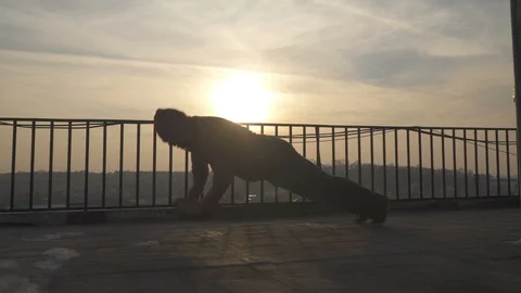 Silhouette of man while doing push ups with clapping hands on terrace in sunset. Video stock 98484460