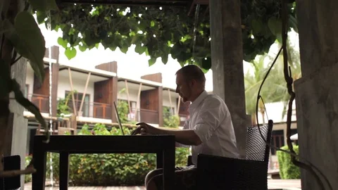 Silhouette of a man working behind a laptop in the hotel garden Stock-Footage 85933933