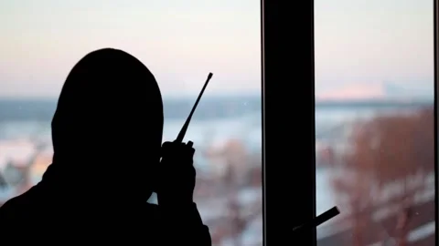 Silhouette of a mantands in front of the window talking into a walkie-talkie Stock Footage 146775779