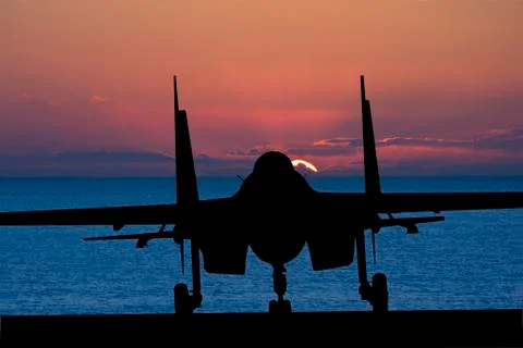Silhouette of military attack aircraft against vibrant sunset sky Stock Photos