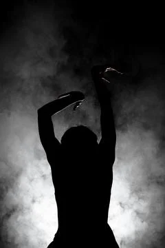 Silhouette modern ballet dancer posing on dark background with smoke Stock Photos