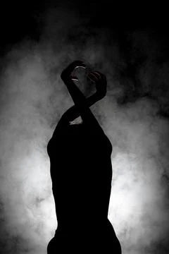 Silhouette modern ballet dancer posing on dark background with smoke Stock Photos