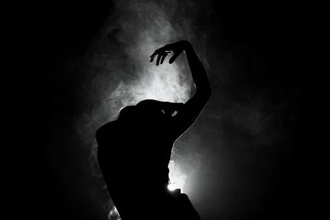 Silhouette modern ballet dancer posing on dark background with smoke Stock Photos