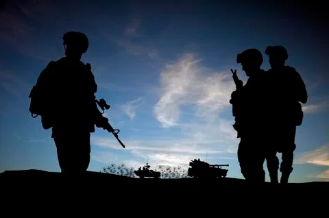 Silhouette of modern soldiers against sunset wky with military vehicles Stock Photos
