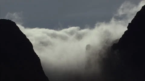 Silhouette of mountains surrounded by clouds settling low on horizon Video stock 202536161