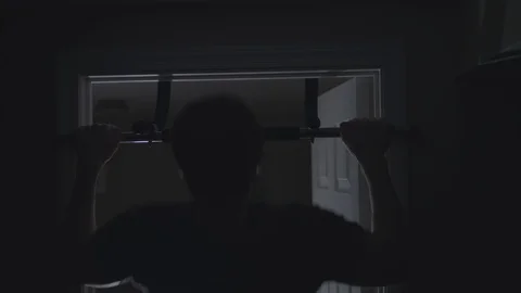 Silhouette of muscular man doing pull-ups on a doorway bar at home in the dark. Stock Footage 86568776