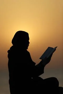 Silhouette of a Muslim woman reading the Noble Quran at sunset, United Arab Stock Photos