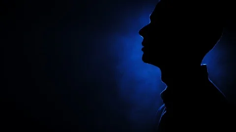 Silhouette of pensive guy standing in the dark smoky room. Bright blue lamp Stock Footage 106471282