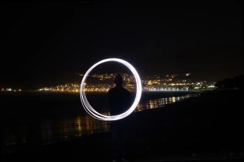 Silhouette of person creating circular light painting on beach at night with  Stock Photos