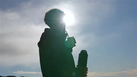 Silhouette of person drinking yerba mate outdoors against bright sky and sun in Stock Footage 328294973