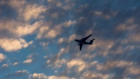 Silhouette of the plane in the clouds at sunset Stock Photos