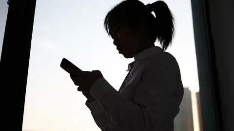 Silhouette of playing mobile Internet chat in front of the window Stock Footage 193994845