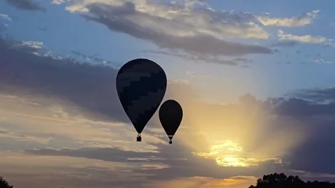 Silhouette profile of two hot air balloons flying in the cloudy sky during a 動画素材 336886950
