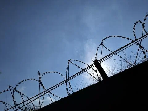 Silhouette of razor wire on a dark wall against a blue sky. Stock Photos