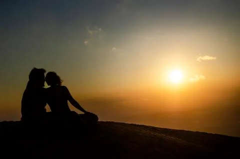 Silhouette of a romantic couple kissing on top of a mountain in the sunset Stock Photos