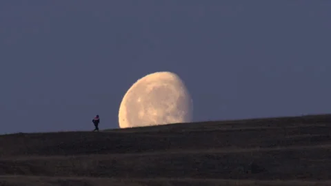 Silhouette of running man on a mountain slope against large moon and night sky Stock Footage 308904366