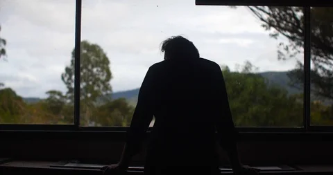 Silhouette of Sad old man at window with mountains in background 스톡 동영상 122348700