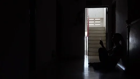 Silhouette of a sad young man reading phone message sitting in the dark Stock Footage 112069941