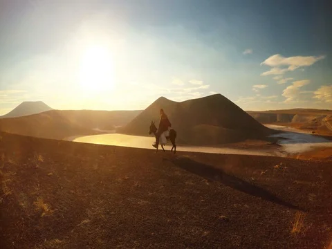 Silhouette of a shepherd riding a mule in the rays of a sunset near a crater Stock Footage 77881063