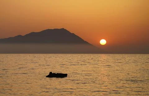 Silhouette shot of a floating object on the ocean during sunset with a mountain 스톡 사진