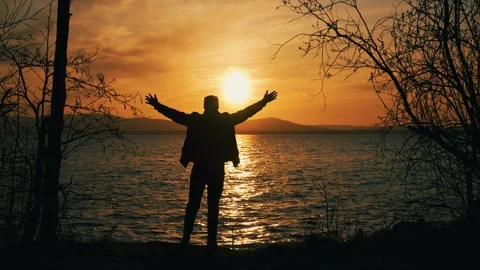 The silhouette of a single man standing on the shore of a lake at sunset. Vidéo 337563433