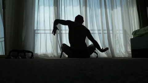 Silhouette of a slender guy in front of a panoramic window meditating and doing Stock Footage 254006792