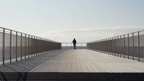 The silhouette of a slender man in a jacket walking along a beautiful wooden pie Stock Footage 121313124