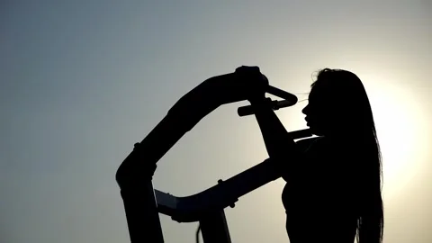 Silhouette of a slender woman on a pull-up simulator on an outdoor sports field. Stock Footage 294353369