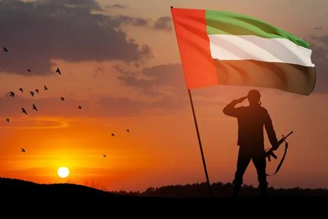 Silhouette of soldier saluting with the flag of UAE on background of the sunset Stock Photos