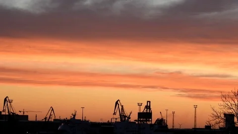 Silhouette of some cranes in the harbor with moving ship at sunrise Stock Footage 106322487
