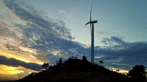 Silhouette of spinning wind turbine crowns hill, sunset backdrop paints the s Stock Footage 243741091
