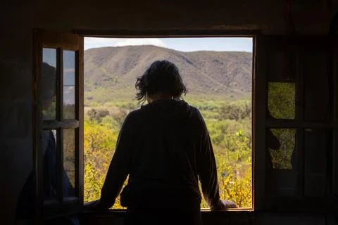 Silhouette stands framed by open window, gazing out Stock Photos