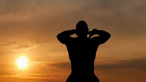 Silhouette of a strong man does a breathing exercise alone at sunset, meditating Stock Footage 114981785