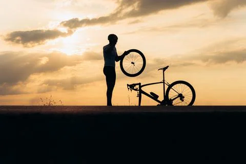 Silhouette of strong man fixing wheel on bike outdoors Stock Photos