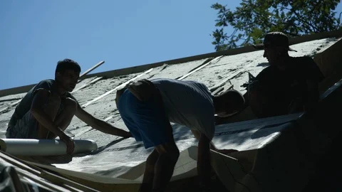 Silhouette of three roofers on rooftop, workers assembling insulation elements. Stock Footage 98757400