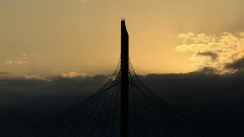 Silhouette of a towering cable-stayed bridge pylon against a striking golden Stock Photos