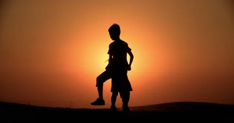 Silhouette of two children of brother and sister having fun playing at sunset Stock Footage