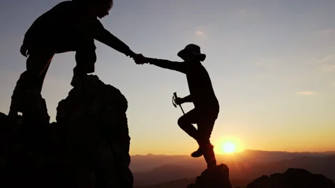 Silhouette of  Two climbers assist one another while scaling a rocky mounta.. Stock Footage 336933467