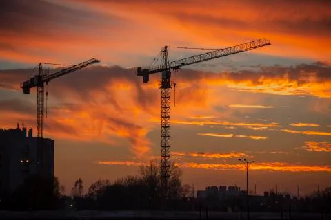 Silhouette of two construction cranes in front of sunset Stock Photos